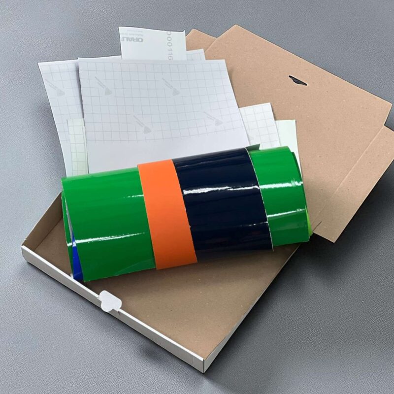 Wir sehen auf einem hellen Hintergrund einen offenen Karton mit bunter Folie.