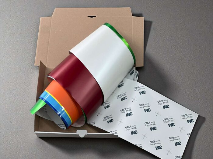 Car Wrapping Restfolien | Bunte Autofolien im Set Mehrere bunte Rollen Autofolie in einer offenen Versandverpackung, darunter auch Folien von 3M mit sichtbarem Rückseitenaufdruck.