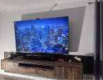 Wandmontierter Fernseher über einem Sideboard, beleuchtet durch weiches LED-Licht mit 30 % Diffusorfolie. Gleichmäßiger Lichtschein an der Wand sichtbar.