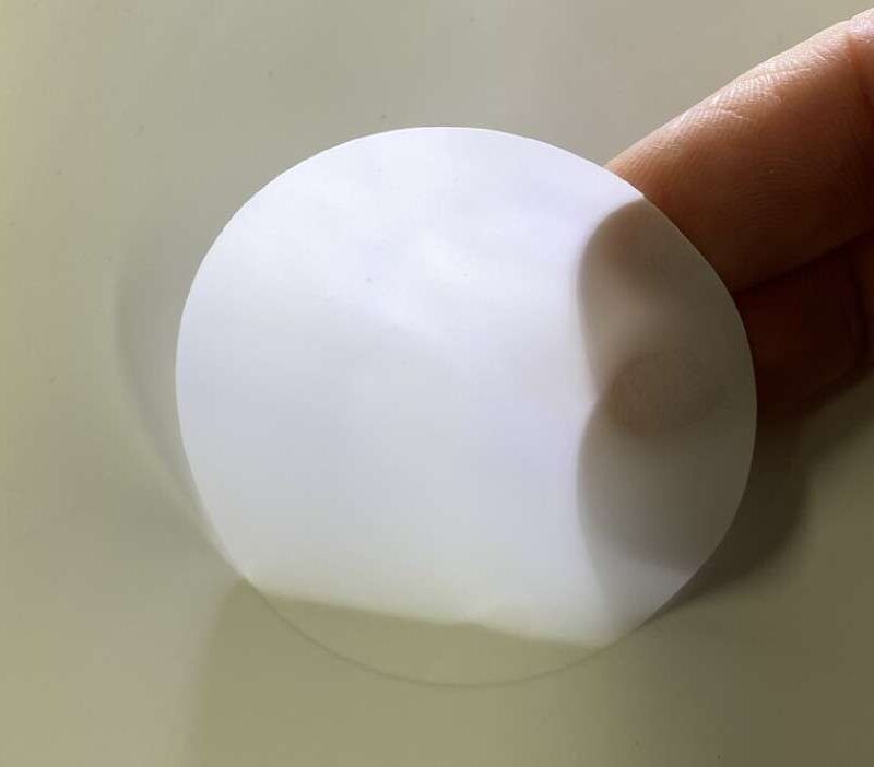 Runder Zuschnitt einer weißen, lichtstreuenden 60 % Diffusorfolie wird von Hand vor hellem Hintergrund gehalten