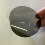 LED-Filterfolie in braungrauem Farbton mit glänzender Oberfläche, wird zwischen zwei Fingern vor hellem Hintergrund gehalten.