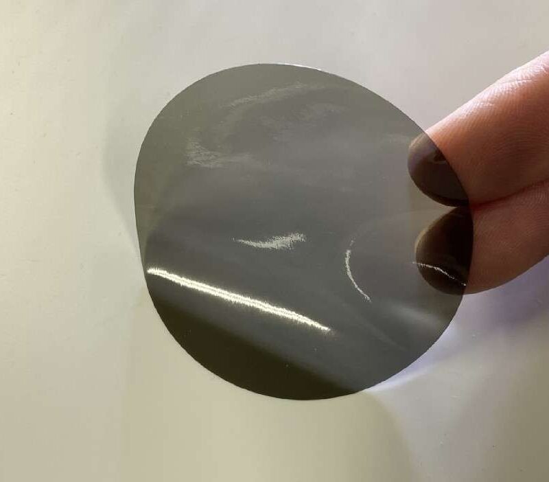 LED-Filterfolie in braungrauem Farbton mit glänzender Oberfläche, wird zwischen zwei Fingern vor hellem Hintergrund gehalten.
