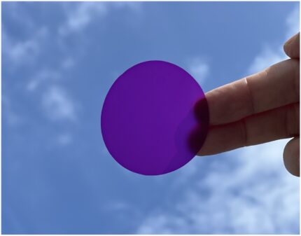 LED-Filterfolie in einem Lila Farbton mit glänzender Oberfläche, wird zwischen zwei Fingern vor einem Himmel mit Wolken.