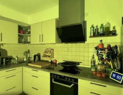 Helle Küche mit vielen Schränken, Herd, Dunstabzugshaube und Küchenutensilien, in ein zitronengelbes Licht getaucht.