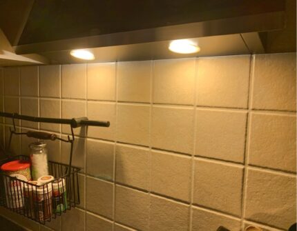 Zwei eingelassene LED-Spots mit einer Diffusorfolie in Beige unter einer Dunstabzugshaube beleuchten eine Küchenrückwand mit Fliesen.