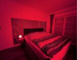 Modernes Schlafzimmer mit Doppelbett und Nachttischlampe, komplett in intensives, tiefrotes Licht getaucht durch eine extrem rote Diffusorfolie.