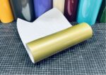 Mactac MACal 9800-100 Gold glänzende Plotterfolie, aufgerollt mit weißem Trägerpapier auf einer karierten Schneidematte