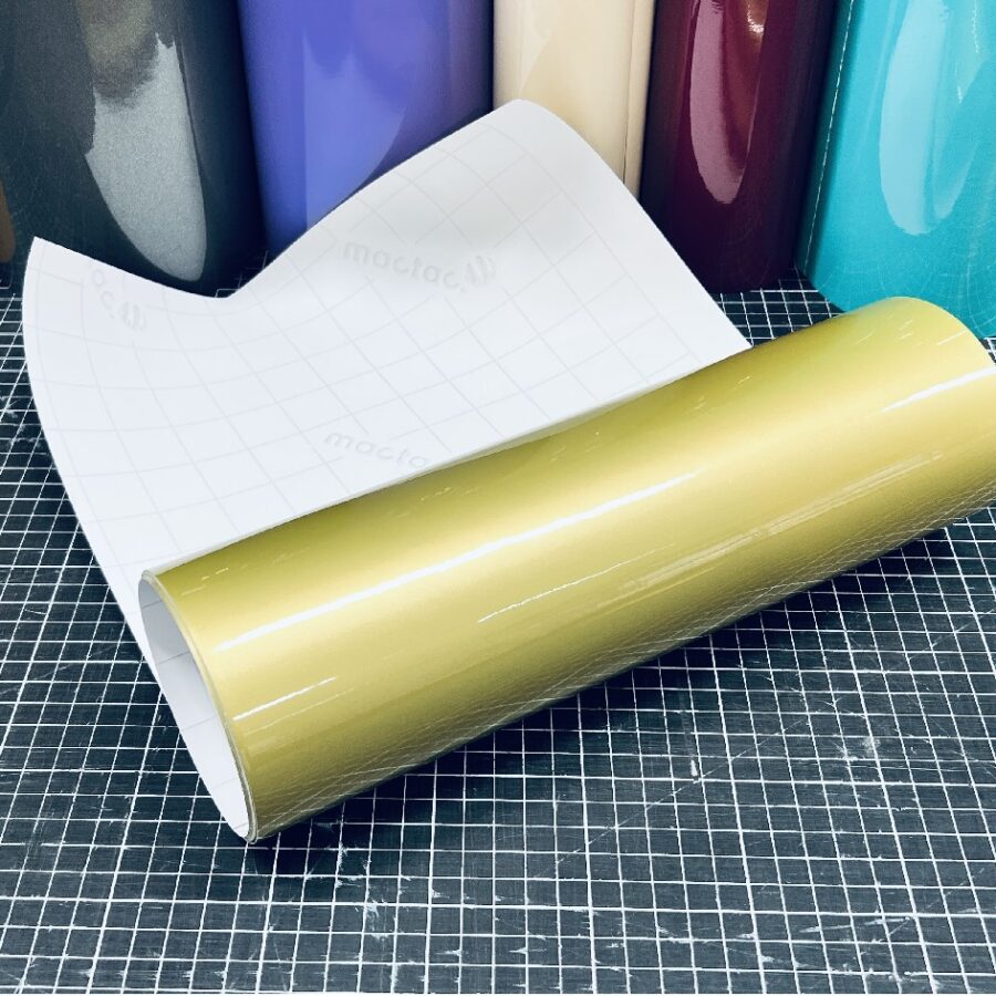 Mactac MACal 9800-100 Gold glänzende Plotterfolie, aufgerollt mit weißem Trägerpapier auf einer karierten Schneidematte