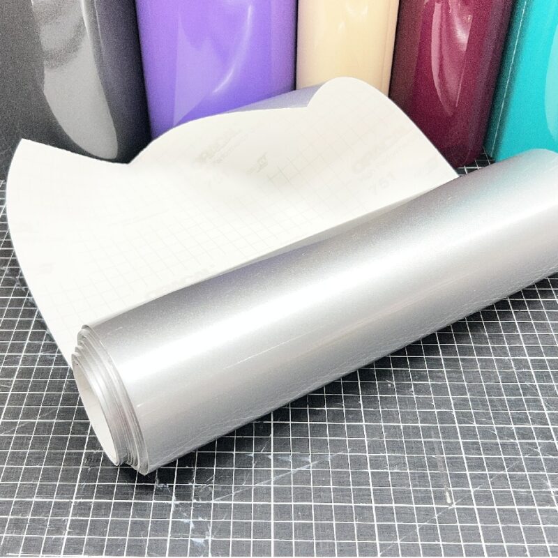 ORACAL 090 Silber glänzende Plotterfolie als aufgerollter Zuschnitt mit weißem Trägerpapier auf einer karierten Schneidematte