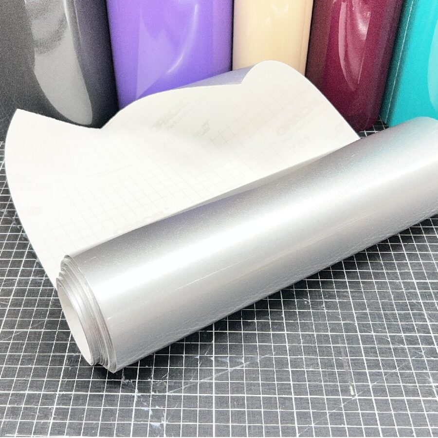 ORACAL 090 Silber glänzende Plotterfolie als aufgerollter Zuschnitt mit weißem Trägerpapier auf einer karierten Schneidematte