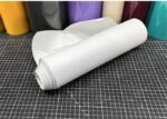ORACAL 751C-010 Weiß matt als aufgerollte Plotterfolie auf einer karierten Schneidematte, mit weißem Trägerpapier und farbigen Folien im Hintergrund